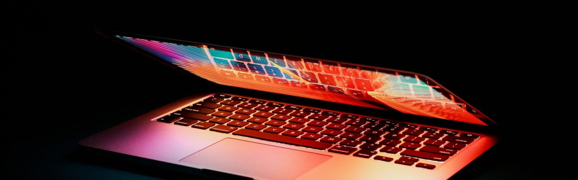 Laptop partially opened, emitting vibrant multicolored lights in dark setting.